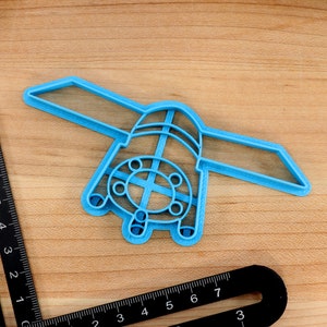 May include: A light blue plastic cookie cutter shaped like a spaceship with a round window and a cross-shaped design in the center.