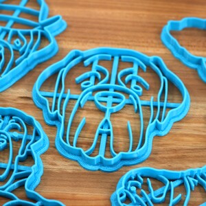 Peut inclure: Un ensemble de cinq emporte-pi&egrave;ces en plastique bleu en forme de diff&eacute;rentes races de chiens. Les emporte-pi&egrave;ces sont sur une surface en bois.