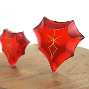 May include: Two red, star-shaped crystal ornaments with gold accents on a wooden base.