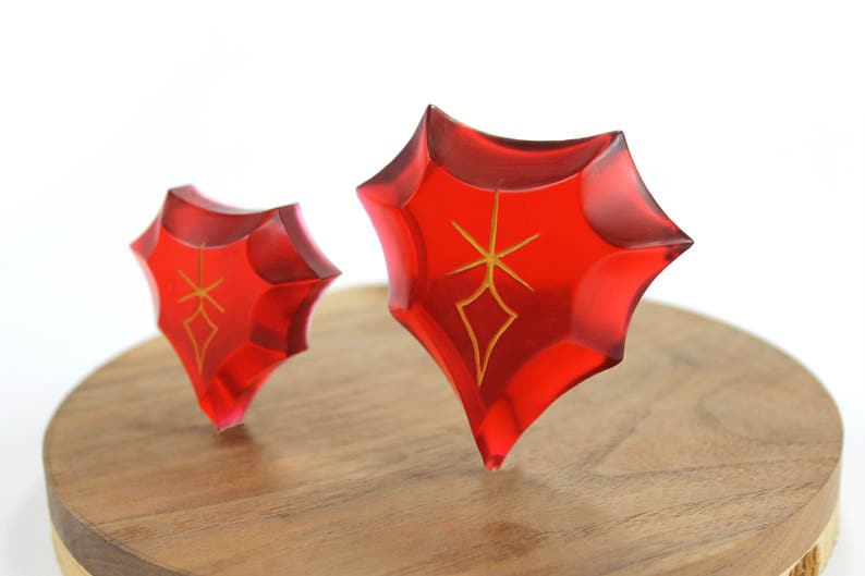 May include: Two red, star-shaped crystal ornaments with gold accents on a wooden base.