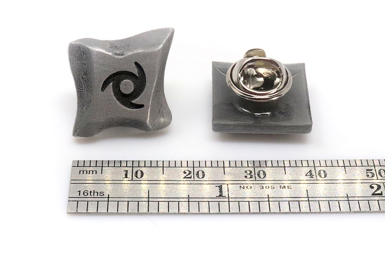 May include: A silver metal pin with a black swirl design. The pin is about 1 inch in diameter and has a safety clasp on the back.