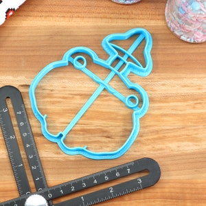 May include: A light blue plastic cookie cutter shaped like a snowman with a hat. The cutter is on a wooden surface.