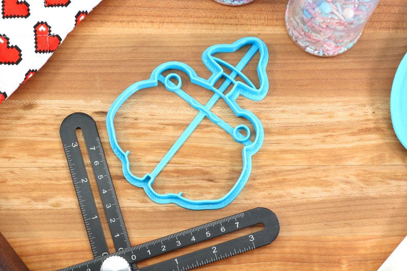 May include: A light blue plastic cookie cutter shaped like a snowman with a hat. The cutter is on a wooden surface.