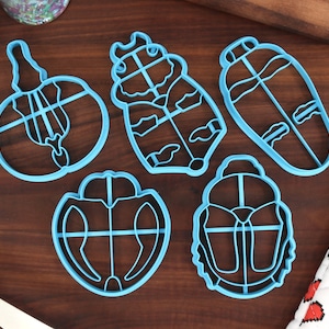 Pode incluir: Conjunto de seis cortadores de biscoitos de plástico azul em forma de escaravelhos. Os cortadores têm detalhes intrincados e são perfeitos para fazer biscoitos únicos.