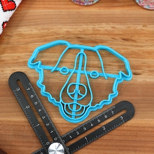May include: A blue plastic cookie cutter shaped like a dog's head. The cutter has a detailed design with a fluffy outline and facial features.