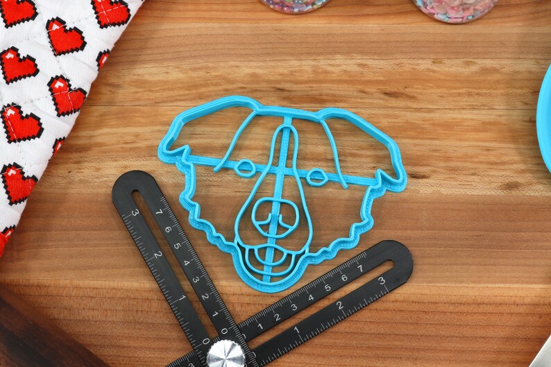 May include: A blue plastic cookie cutter shaped like a dog's head. The cutter has a detailed design with a fluffy outline and facial features.