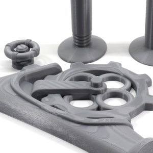May include: A set of gray 3D printed gears and a lever, with a round knob and two cylindrical bases. The gears are interlocked and have a detailed design.