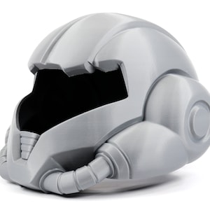 Puede incluir: Un casco de plástico gris con un diseño futurista. El casco tiene una visera grande y una serie de tubos y respiraderos.