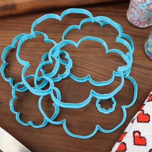 May include: A set of five blue plastic cookie cutters shaped like clouds. The cutters are arranged in a pile on a wooden surface.