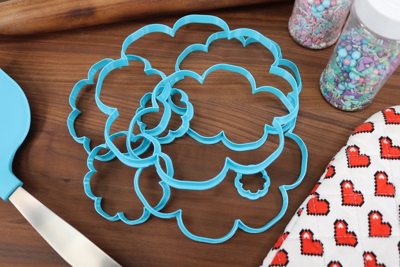 May include: A set of five blue plastic cookie cutters shaped like clouds. The cutters are arranged in a pile on a wooden surface.