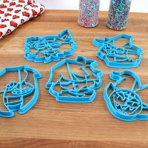 May include: Set of five blue plastic cookie cutters shaped like cartoon characters. The characters include a pirate, a monster, a ghost, a mermaid, and a kraken.