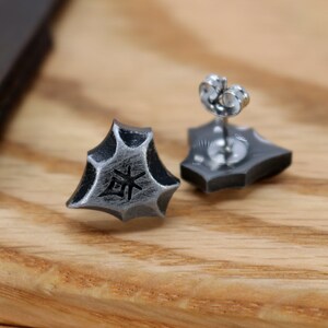 May include: A pair of silver stud earrings with a geometric design. The earrings feature a small, engraved symbol on the front.
