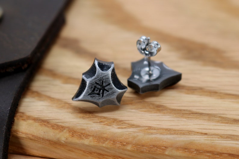 May include: A pair of silver stud earrings with a geometric design. The earrings feature a small, engraved symbol on the front.