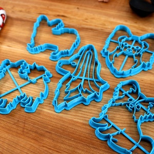 May include: A set of five blue plastic cookie cutters shaped like different dog breeds. The cutters are on a wooden surface.