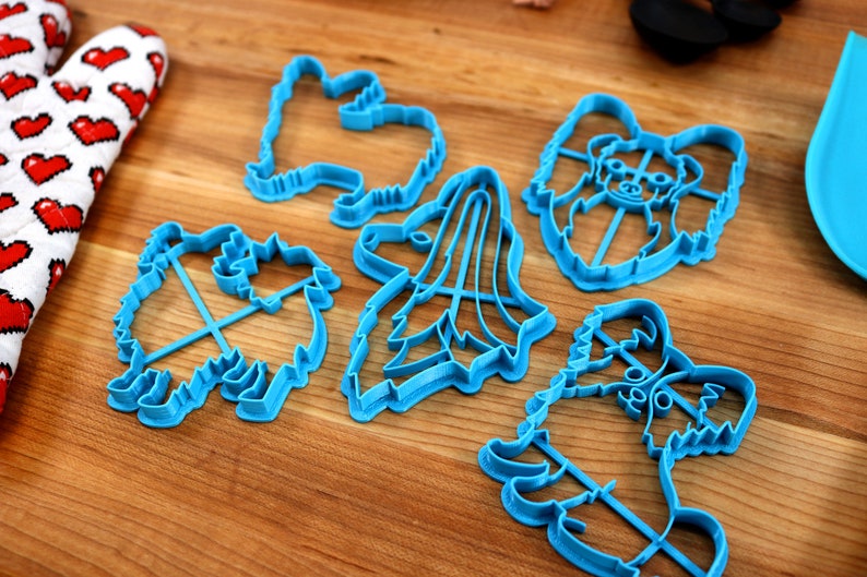 May include: A set of five blue plastic cookie cutters shaped like different dog breeds. The cutters are on a wooden surface.