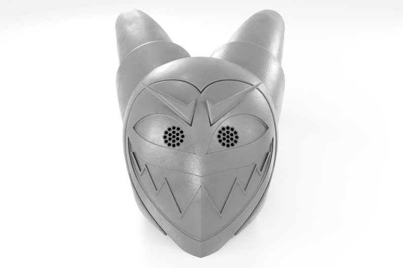 May include: A silver-colored helmet with a menacing expression, featuring two large, round eyes with black mesh details and a jagged, toothy grin.