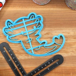 May include: A blue plastic cookie cutter shaped like an axolotl with a heart on its tail.