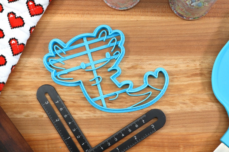 May include: A blue plastic cookie cutter shaped like an axolotl with a heart on its tail.