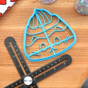 May include: A blue plastic cookie cutter shaped like a cartoon poo emoji wearing a hat. The cutter is on a wooden surface.