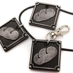 May include: Three silver-colored pendants with a black background and a stylized cloud design. The pendants are attached to a black cord with a silver clasp.