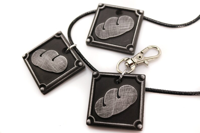 May include: Three silver-colored pendants with a black background and a stylized cloud design. The pendants are attached to a black cord with a silver clasp.