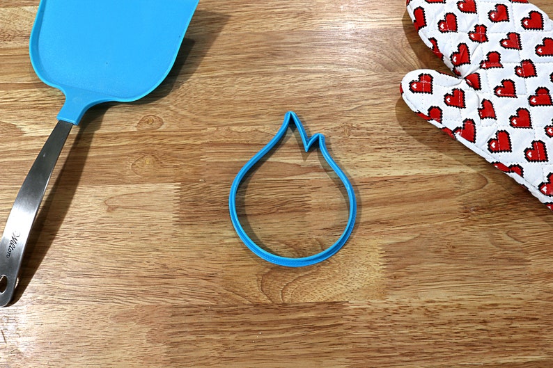 May include: A blue plastic cookie cutter shaped like a flame on a wooden surface.