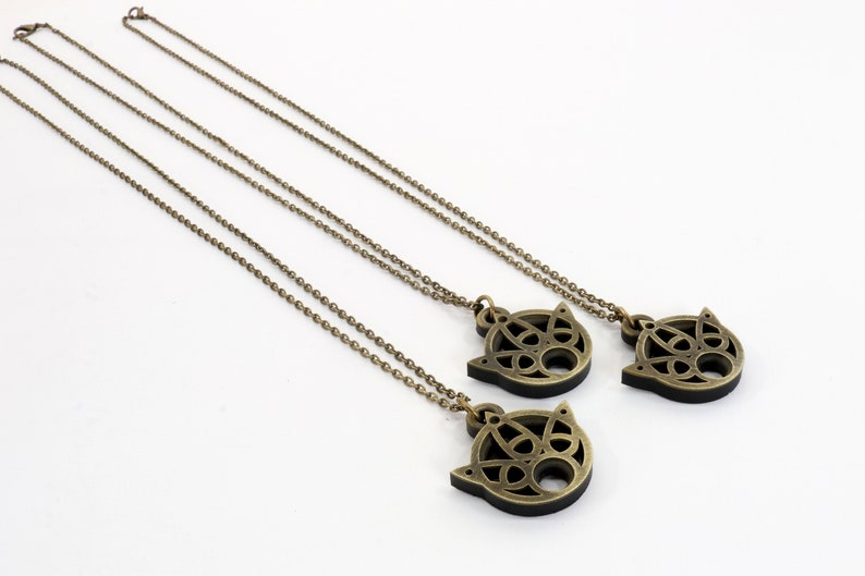 May include: Three gold necklaces with intricate, circular, Celtic-style pendants. The pendants are in the shape of a cat's face.