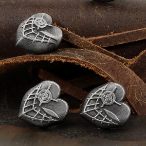 May include: Three silver heart-shaped charms with a geometric design. The charms are on a brown leather background.
