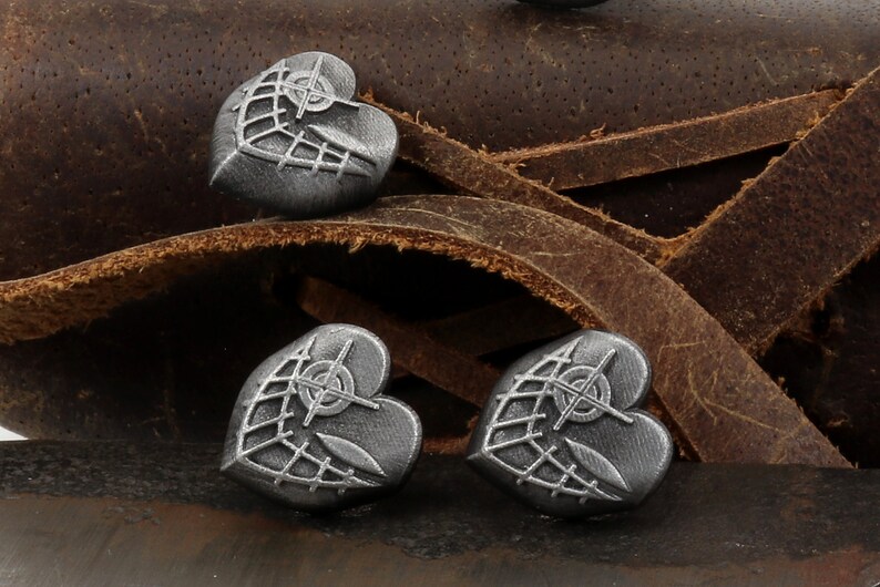 May include: Three silver heart-shaped charms with a geometric design. The charms are on a brown leather background.