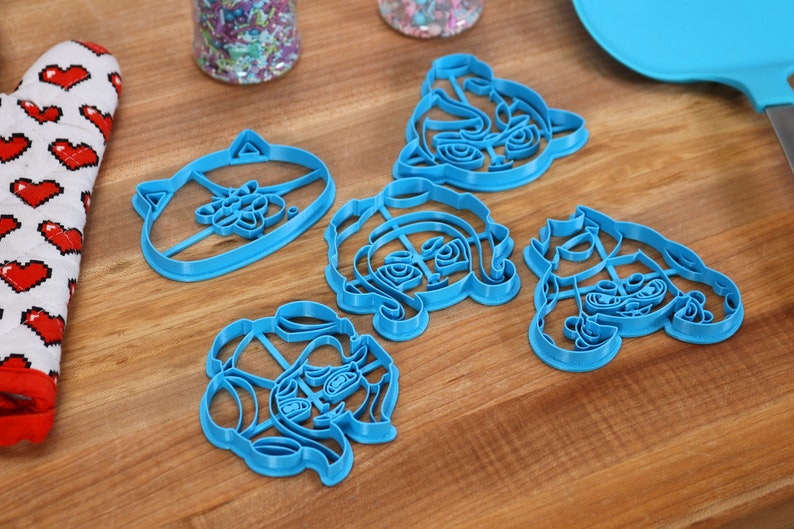 May include: Set of five blue plastic cookie cutters shaped like cartoon animal faces.