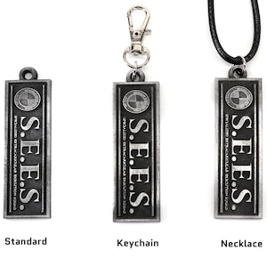 May include: Three silver metal pendants with the text "S.E.E.S. SPECIALIZED EXTRACARKULAR EXECUTION SQUAD" and a logo. The pendants are shown in three variations: standard, keychain, and necklace.