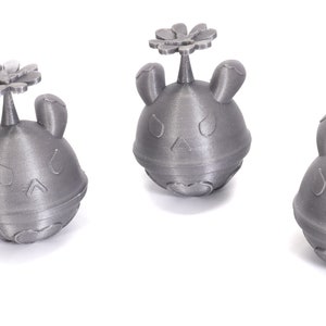 May include: Three silver-colored 3D printed figurines of a cartoon character with a flower on top. The character has a round body, two ears, and a face with two eyes and a mouth.