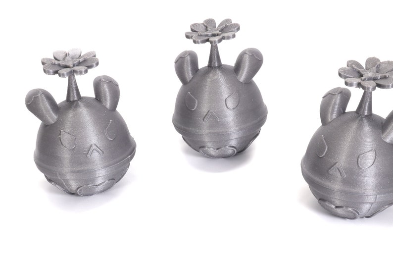 May include: Three silver-colored 3D printed figurines of a cartoon character with a flower on top. The character has a round body, two ears, and a face with two eyes and a mouth.