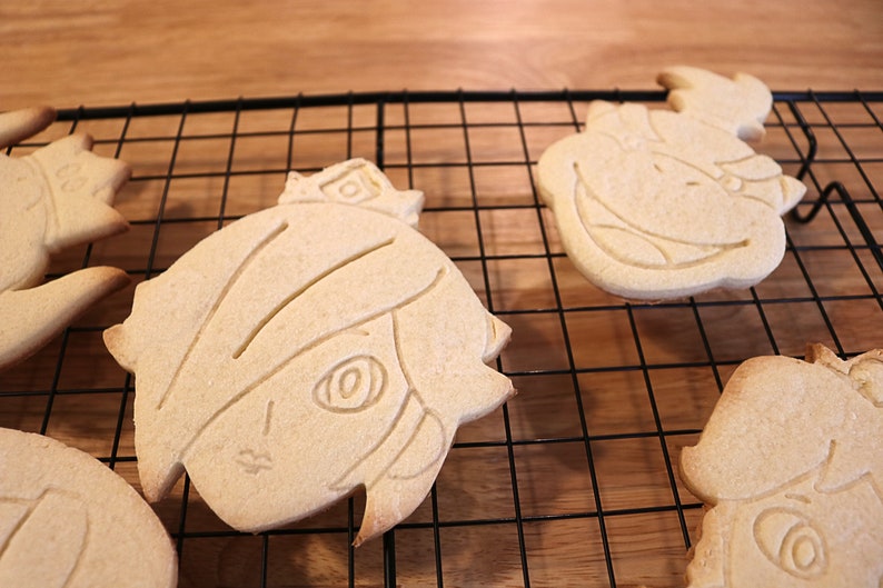 May include: Four sugar cookies on a wire rack. The cookies are shaped like cartoon characters with detailed facial features.