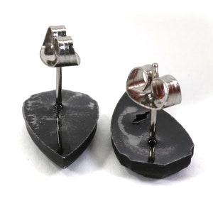 May include: A pair of black stud earrings with silver posts and backs. The earrings are shaped like a teardrop.