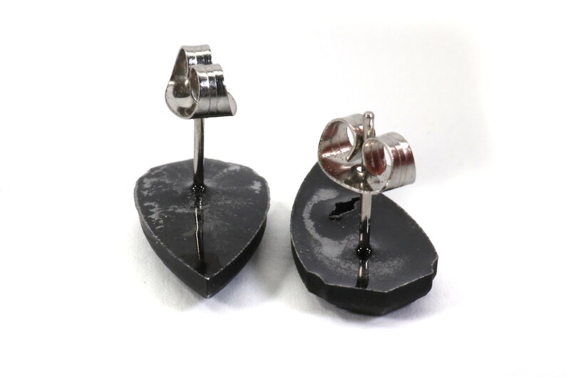 May include: A pair of black stud earrings with silver posts and backs. The earrings are shaped like a teardrop.
