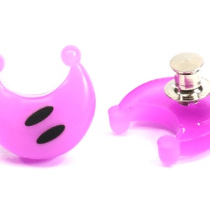 May include: Two purple crescent moon shaped plastic buttons with black eyes. One button has a silver pin back.