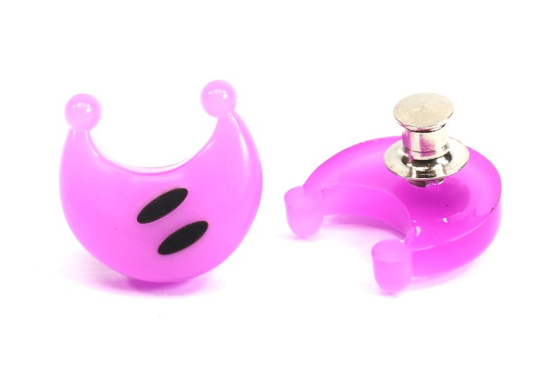 May include: Two purple crescent moon shaped plastic buttons with black eyes. One button has a silver pin back.