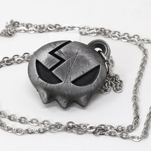 May include: A silver necklace with a pendant shaped like a skull with a cracked face and a lightning bolt on the forehead.