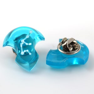 May include: A blue plastic pin with a white constellation design. The pin has a metal clasp on the back.