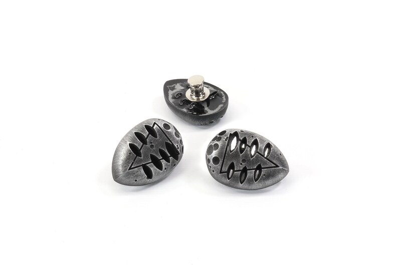 May include: Three silver-colored metal buttons with a black design. Each button features a stylized tree design with a triangular shape and leaf-like details.