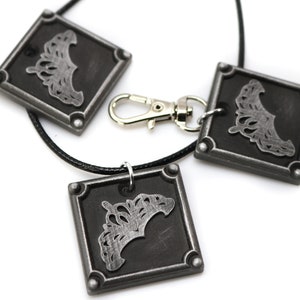May include: Three silver-toned square pendants with a crown design on a black cord necklace. The necklace has a silver-toned lobster clasp.