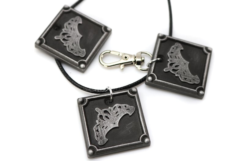 May include: Three silver-toned square pendants with a crown design on a black cord necklace. The necklace has a silver-toned lobster clasp.