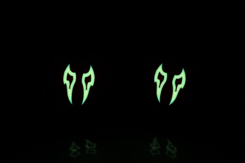 May include: Two glow-in-the-dark green flame-shaped earrings. The earrings are on a black background.