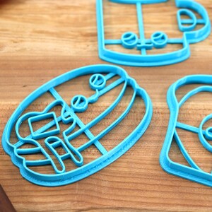 May include: A set of blue plastic cookie cutters shaped like a coffee cup, a donut, a hamburger, and a loaf of bread. The cutters are on a wooden surface.