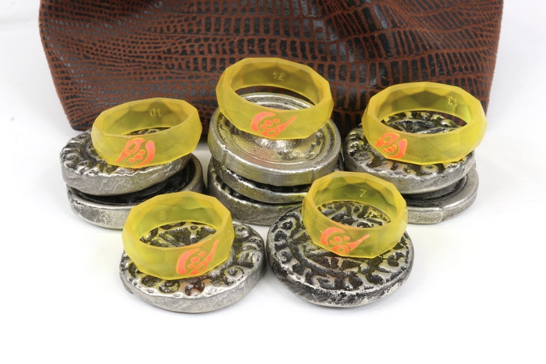 May include: A set of eight yellow silicone rings with a red design. The rings are stacked on top of silver coins.