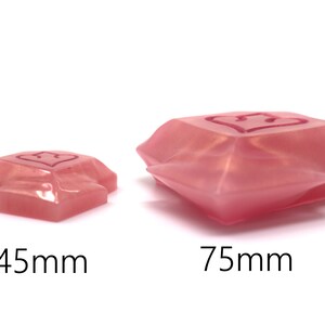 May include: Two pink, heart-shaped resin objects. The smaller one is 45mm, and the larger one is 75mm. Each has a heart design etched on the top surface. The objects have a faceted, gem-like appearance, and are set against a white background.