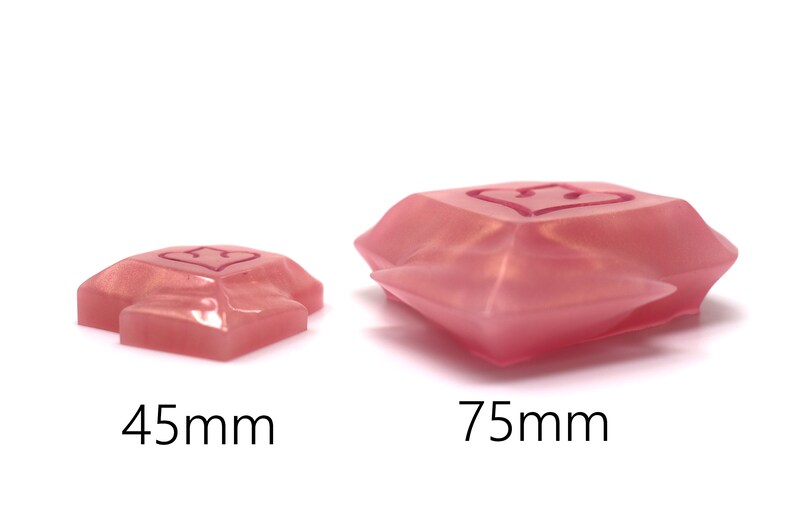 May include: Two pink, heart-shaped resin objects. The smaller one is 45mm, and the larger one is 75mm. Each has a heart design etched on the top surface. The objects have a faceted, gem-like appearance, and are set against a white background.