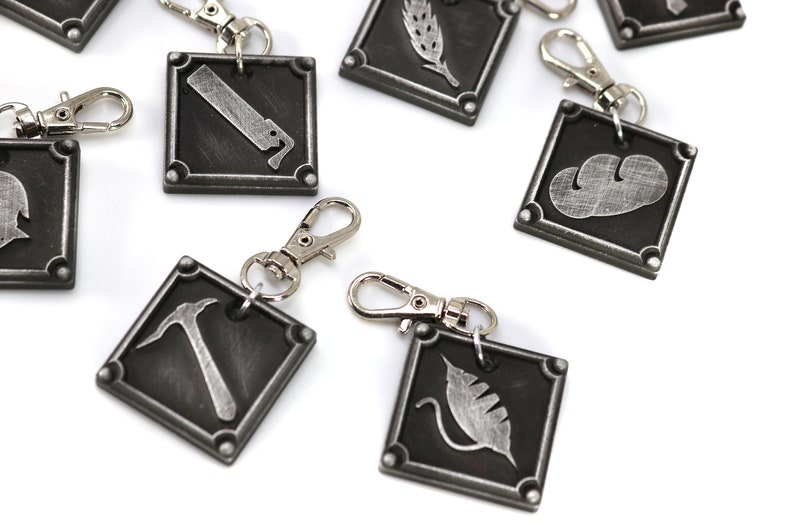May include: Set of eight silver keychains with different symbols on black square metal tags. The symbols include a hammer, a leaf, a wheat stalk, a knife, a cloud, and a helmet.