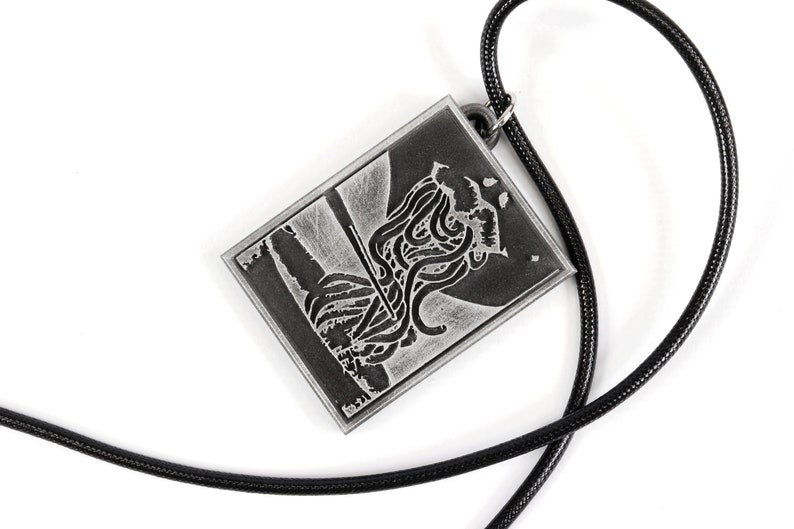 May include: A silver pendant necklace with a black cord. The pendant features a detailed image of a creature with tentacles.
